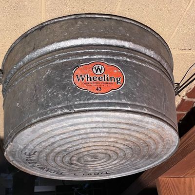 Vintage Wheeling Corrugating Company galvanized metal wash tub, featuring the original red and white paper label and wire handles.