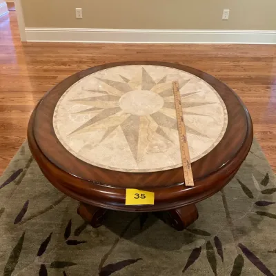Sale Photo Thumbnail #12: Round wooden coffee table featuring a polished stone inlay with a compass rose design, supported by a sturdy pedestal base.