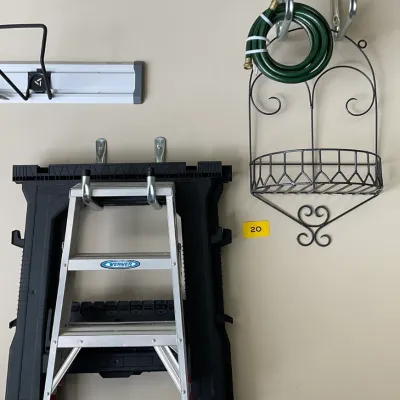 Sale Photo Thumbnail #5: Assorted garage and garden items including a Werner aluminum step ladder, a black plastic folding sawhorse, a coiled green garden hose, and a decorative metal wall basket.
