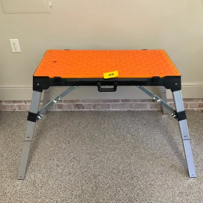 Sale Photo Thumbnail #6: Centipede portable work stand with an orange and black folding tabletop, supported by adjustable aluminum legs.
