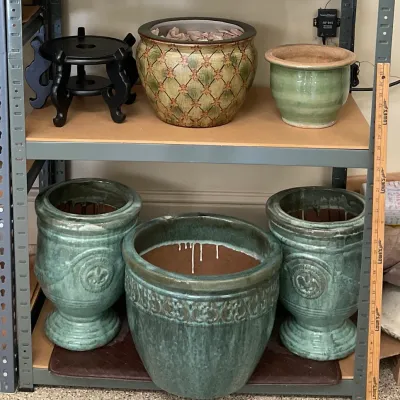 Sale Photo Thumbnail #4: Collection of ceramic planters, including a pair of green glazed urn-style pots with fleur-de-lis details, a large green glazed pot, a patterned fishbowl planter, and a black wooden stand.