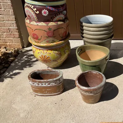Sale Photo Thumbnail #27: Assortment of ceramic garden planters, including a stack of three large, vibrantly painted bohemian-style pots, a stack of grey glazed pots, and several rustic terracotta-style planters.