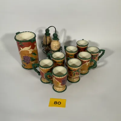 Sale Photo Thumbnail #22: Tuscan-style ceramic tableware set featuring a wine cooler, oil and vinegar cruets in a metal stand, and seven matching mugs decorated with grape and olive motifs.