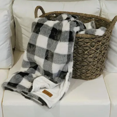 Sale Photo Thumbnail #63: Plush black, grey, and white buffalo plaid throw blanket by Koolaburra by UGG drape over a large woven seagrass storage basket.