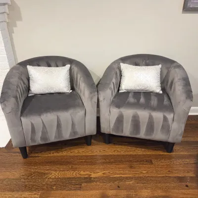 Sale Photo Thumbnail #47: Pair of contemporary grey velvet barrel accent chairs, each with a patterned silver throw pillow and dark tapered legs.