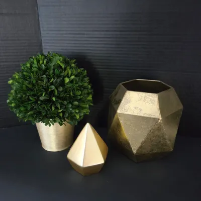 Sale Photo Thumbnail #122: Modern gold-tone decorative accent set featuring a artificial boxwood topiaries in a textured gold pot, a geometric faceted object, and a matching faceted planter or vase.