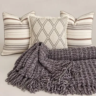 Sale Photo Thumbnail #79: Set of three neutral throw pillows featuring striped and geometric fringe designs, paired with a chunky dark grey chenille knit blanket with tassel trim.