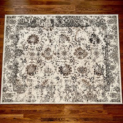 Sale Photo Thumbnail #96: Traditional Persian-style area rug featuring a distressed floral and medallion design in ivory and charcoal tones, laid flat on dark hardwood flooring.