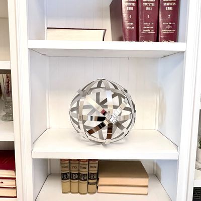 Sale Photo Thumbnail #102: Contemporary polished chrome metal strap sphere decorative sculpture displayed on a white bookcase shelf among vintage hardback books and 1981 Oklahoma Statutes legal volumes.
