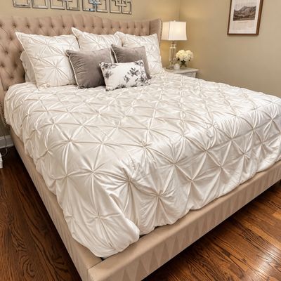 Sale Photo Thumbnail #85: Upholstered wingback bed set featuring a beige tufted headboard with nailhead trim and an ivory pintuck comforter with matching pillows.