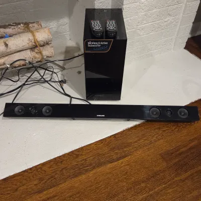 Sale Photo Thumbnail #71: Samsung soundbar speaker system with a wireless active subwoofer and two remote controls.