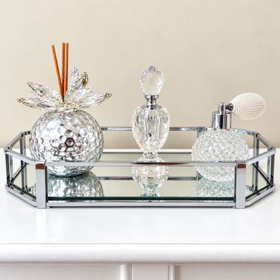 Sale Photo Thumbnail #130: Octagonal chrome and mirrored vanity tray holding cut crystal perfume bottles and a metallic diffuser vessel with crystal accents.