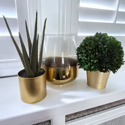 Sale Photo Thumbnail #124: Trio of modern decorative home accents, including two potted artificial plants in metallic gold planters and a smoked glass vase with a reflective gold base.