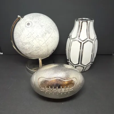 Sale Photo Thumbnail #65: Trio of modern decorative items, including a white and silver desk globe, a metallic football figure, and a white ceramic vase with silver geometric outlines.