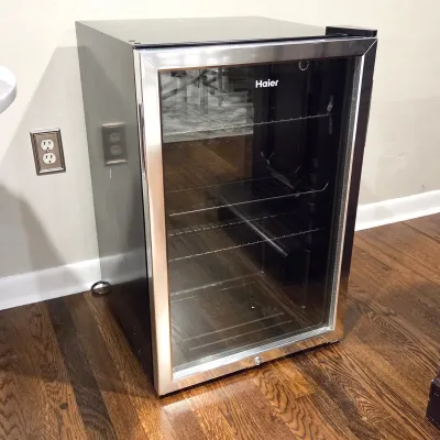 Sale Photo Thumbnail #70: Haier freestanding mini beverage refrigerator featuring a stainless steel trimmed glass door, black cabinet, and adjustable wire shelving.