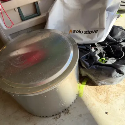 Sale Photo Thumbnail #99: Solo Stove stainless steel fire pit with lid, accompanied by its white protective cover and black carrying bag.