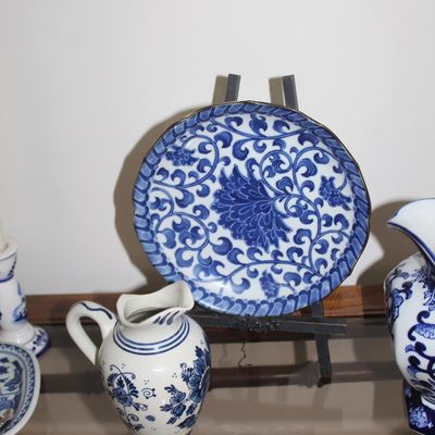 Sale Photo Thumbnail #9: Vintage blue and white porcelain decorative plate with floral scrollwork on a display stand, accompanied by a matching small pitcher.