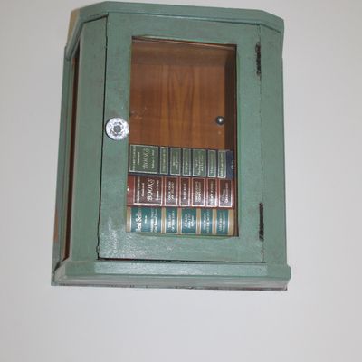 Sale Photo Thumbnail #47: Vintage wall-mounted wooden cabinet painted sage green, featuring a glass door with a crystal knob and containing three Reader's Digest Condensed Books.