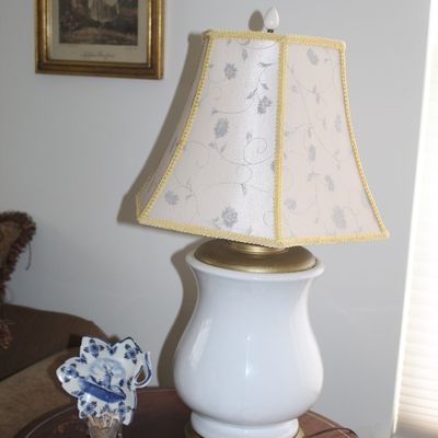 Sale Photo Thumbnail #20: Vintage white ceramic urn-style table lamp with gold-toned accents and a floral fabric shade, displayed on an inlaid wooden side table alongside small collectibles.