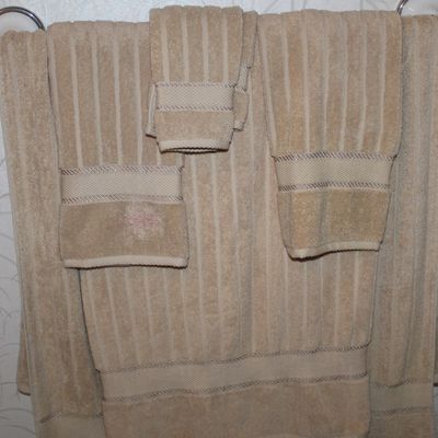 Sale Photo Thumbnail #117: Set of beige ribbed cotton bath towels, hand towels, and a washcloth hanging on a towel bar, showing some discoloration on the left hand towel.