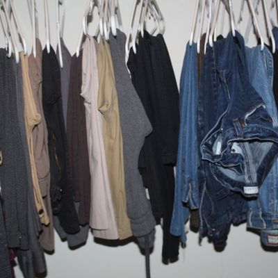Sale Photo Thumbnail #112: Assorted clothing items, including shirts, sweaters, and denim jeans, hanging on white plastic hangers in a closet.
