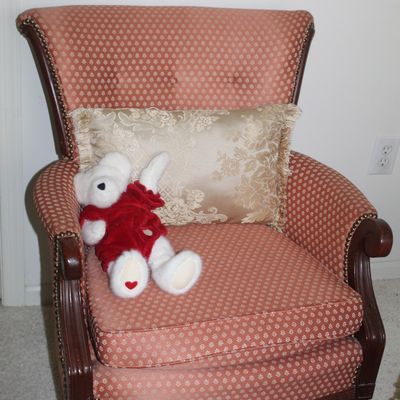 Sale Photo Thumbnail #48: Vintage wingback armchair with pink and gold patterned upholstery, brass nailhead trim, a decorative gold throw pillow, and a plush white teddy bear.