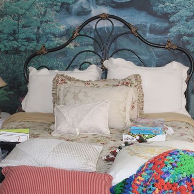 Sale Photo Thumbnail #52: Ornate black metal headboard with gold accents, shown with a variety of floral and patterned bedding, accent pillows, and a colorful crocheted throw blanket.