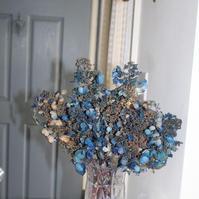 Sale Photo Thumbnail #29: Dried blue hydrangea arrangement in a clear cut-glass vase, displayed alongside a small pink glass trinket dish with brass trim.