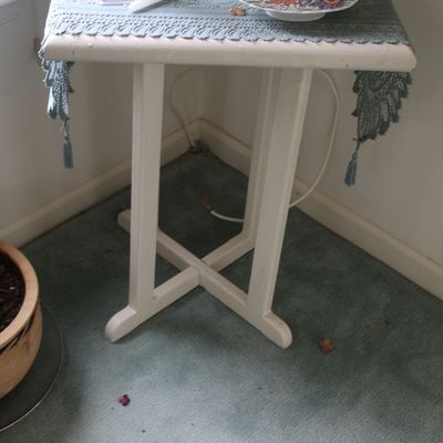 Sale Photo Thumbnail #77: Small white wooden accent table with an X-stretch base, topped with a blue lace runner, a crystal candlestick, and a decorative floral plate.