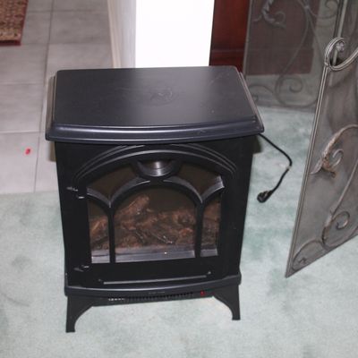 Sale Photo Thumbnail #15: Compact electric fireplace stove heater in a matte black finish, featuring an arched glass viewing window and faux logs.