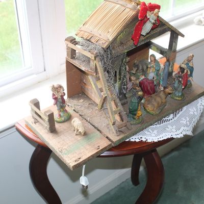 Sale Photo Thumbnail #88: Vintage wooden nativity stable with straw roof and a collection of painted plaster figurines, displayed on a small wooden side table.
