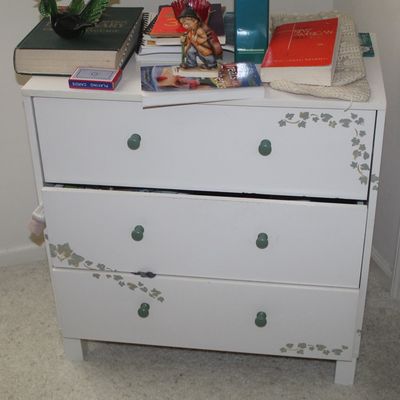 Sale Photo Thumbnail #42: White three-drawer chest featuring green knobs and stenciled ivy leaf details, topped with books and decorative items.