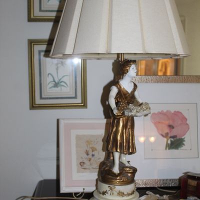 Sale Photo Thumbnail #113: Vintage porcelain and gilt metal figural table lamp depicting a woman carrying a basket, paired with a pleated cream lampshade.