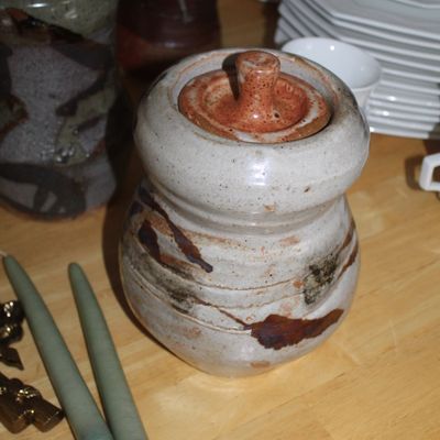 Sale Photo Thumbnail #61: Handcrafted studio pottery lidded jar with a speckled white glaze and brown abstract brushwork, accompanied by two green taper candles.