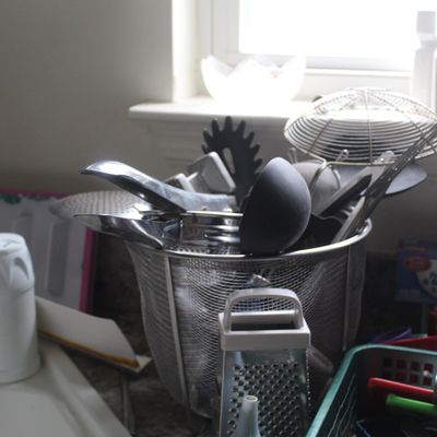 Sale Photo Thumbnail #98: Assorted kitchen utensils including ladles, spatulas, and a mesh strainer, stored in a wire mesh holder alongside a small hand grater.