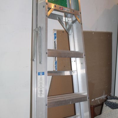 Sale Photo Thumbnail #59: Aluminum A-frame stepladder with a green plastic top cap and utility tray, showing light wear from use.