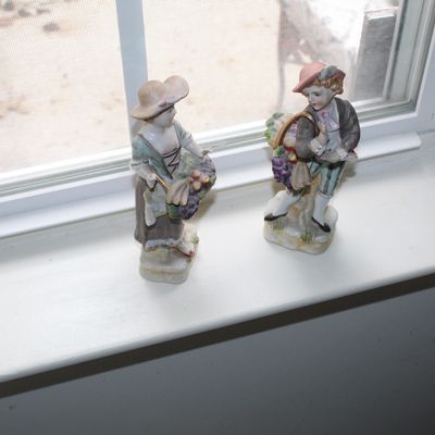 Sale Photo Thumbnail #109: Pair of vintage porcelain figurines depicting a boy and girl in rustic attire carrying baskets of fruit, displayed on a windowsill.