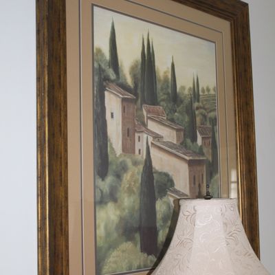 Sale Photo Thumbnail #85: Framed Tuscan landscape print featuring villas and cypress trees, presented in a wide, ornate gold-toned wooden frame with double matting.