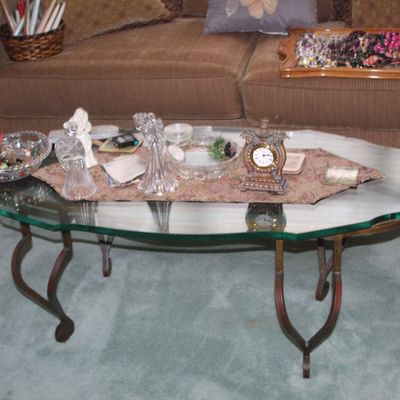 Sale Photo Thumbnail #36: Vintage oval glass-top coffee table with a scalloped edge and curved metal legs, displaying various decorative items including crystal figurines and a small table clock.