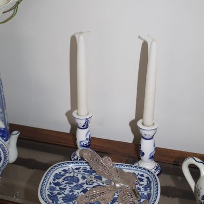 Sale Photo Thumbnail #10: Pair of Delft-style blue and white ceramic candlesticks with white taper candles, accompanied by a matching rectangular floral dish holding a silver glitter butterfly ornament.
