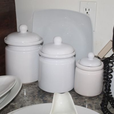 Sale Photo Thumbnail #104: Set of four white ceramic kitchen canisters with matching lids, shown alongside various white serving dishes and a glass bowl.