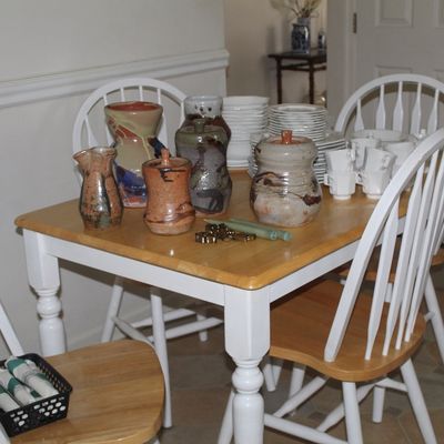 Sale Photo Thumbnail #90: Two-tone wooden dining table with white legs and four matching Windsor-style chairs, displaying an assortment of studio pottery and white ceramic dishware.