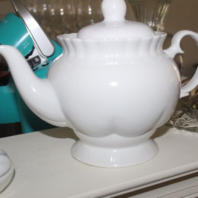 Sale Photo Thumbnail #93: White ceramic teapot with a scalloped rim, pedestal base, and matching lid, shown alongside a teal Keurig coffee maker.
