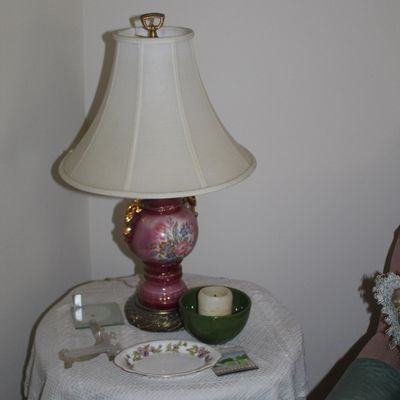 Sale Photo Thumbnail #111: Vintage hand-painted floral porcelain table lamp with gold-tone accents and a white bell shade, displayed on a lace-covered accent table alongside a small decorative plate and a candle bowl.
