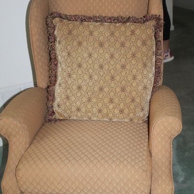 Sale Photo Thumbnail #16: Traditional wingback reclining armchair in a tan patterned upholstery, paired with a coordinating fringed accent pillow.