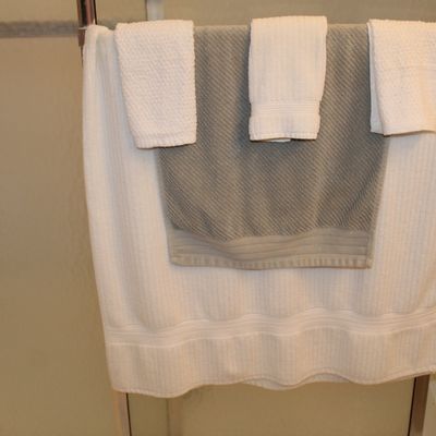Sale Photo Thumbnail #114: Assorted bath towels in white and gray, neatly folded and hanging on a metal towel rack.