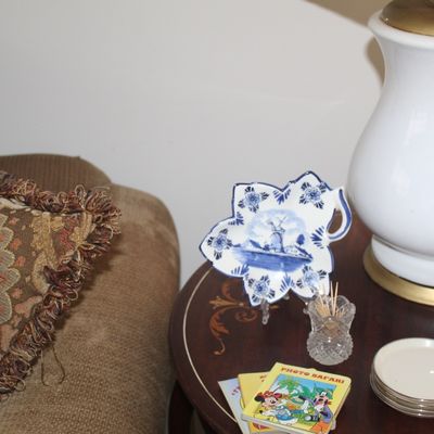 Sale Photo Thumbnail #21: Delft blue and white leaf-shaped porcelain dish with a windmill scene, displayed on a wooden side table alongside a white ceramic lamp and vintage Disney coasters.