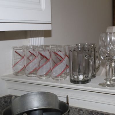 Sale Photo Thumbnail #96: Assorted glassware including mid-century tumblers with red and white spiral patterns, heavy glass beer mugs, and stemmed wine glasses.