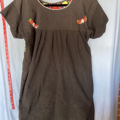 Sale Photo Thumbnail #395: Black short-sleeve embroidered Mexican huipil tunic dress featuring colorful floral embroidery across the neckline, chest, and front lower panel. Features a scoop neckline with stitch details and side vents at the hem. Measures approximately 35 inches in 