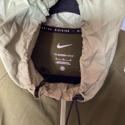 Sale Photo Thumbnail #486: Men's Nike Running Division Therma-Fit hooded full-zip jacket in olive green with patterned light green panels and sleeves. Style code DD6102-386. Features front hand pockets, adjustable hood drawstrings, and reflective Nike swoosh logo on the chest. Size